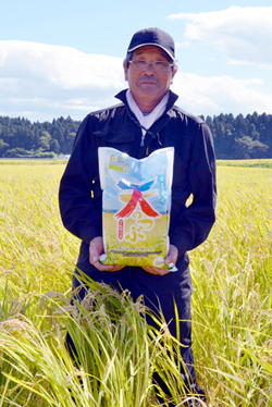 天のつぶのほ場にて米袋を手にPRするJAそうまの佐藤保彦稲作部会長